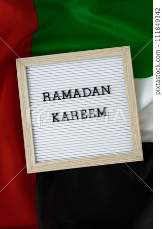Congratulations with text RAMADAN KAREEM - happy holidays waving UAE flag on background concept. Commemoration Day Muslim Greeting card advertisement. Blessed holy month holiday Congratulations with text RAMADAN KAREEM - happy holidays waving UAE flag on background concept. Commemoration Day Muslim Greeting card advertisement. Blessed holy month holiday 111849342