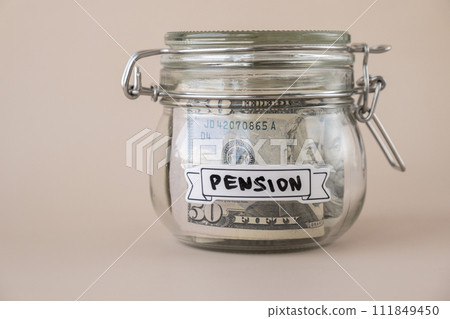 Glass jar full of American currency dollars cash banknote with text PENSION. Preparation saving money. Moderate consumption and economy Glass jar full of American currency dollars cash banknote with text PENSION. Preparation saving money. Moderate consumption and economy 111849450