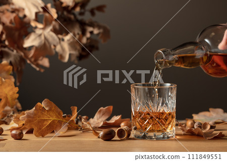 Whiskey with ice on a wooden table with dried-up oak leaves. 111849551