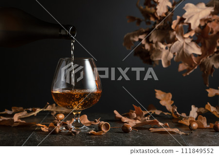 Brandy is poured from a bottle into a glass. Brandy is poured from a bottle into a glass. 111849552