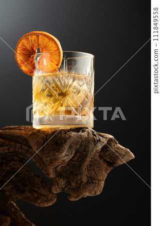 Old fashioned cocktail with ice and dried orange slice on a old snag. Old fashioned cocktail with ice and dried orange slice on a old snag. 111849558