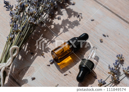 Glass bottle dropper with dried lavender flowers. Wild harvested essential oil beauty product. Organic herbs skincare ingredient environmentally friendly Glass bottle dropper with dried lavender flowers. Wild harvested essential oil beauty product. Organic herbs skincare ingredient environmentally friendly 111849574