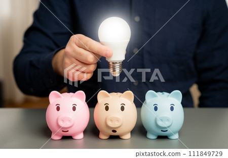 Businessman holding a light bulb over a piggy bank. Choose the best investment idea. New ways to save money. Invest. Open a deposit. Invest in business. Ingenuity and creativity. Eureka moment Businessman holding a light bulb over a piggy bank. Choose the best investment idea. New ways to save money. Invest. Open a deposit. Invest in business. Ingenuity and creativity. Eureka moment 111849729