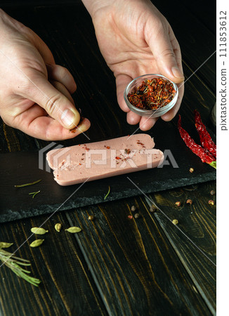 The cook prepares aromatic sausage with spices on the kitchen table. Chef hand adding dry seasoning to raw sausage before baking 111853612