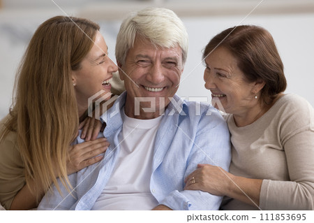 Happy mature wife and adult daughter hugging senior dad Happy mature wife and adult daughter hugging senior dad 111853695