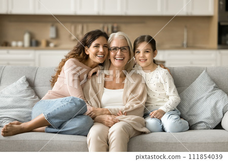 Happy grandma, mom and granddaughter kid sitting close on sofa Happy grandma, mom and granddaughter kid sitting close on sofa 111854039