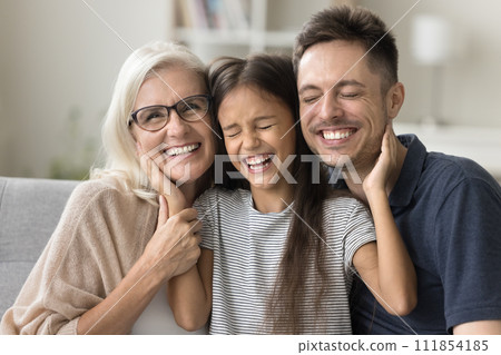Cheerful sweet girl resting on couch between dad and grandma Cheerful sweet girl resting on couch between dad and grandma 111854185