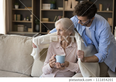Adult son covering his mature mother with warm plaid Adult son covering his mature mother with warm plaid 111854201