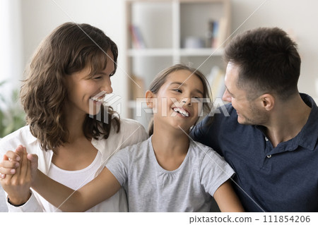 Cheerful young parents and happy carefree child girl sitting together Cheerful young parents and happy carefree child girl sitting together 111854206