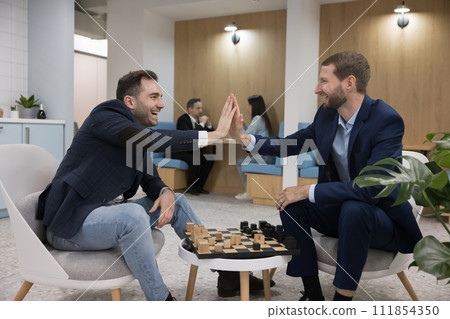 Two smiling colleagues giving high five play chess in coworking Two smiling colleagues giving high five play chess in coworking 111854350