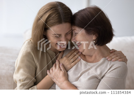 Joyful senior mom and adult daughter hugging, chatting 111854384