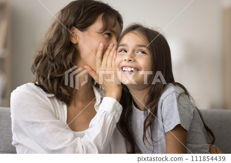 Happy playful mother telling secret to cute pretty girl kid Happy playful mother telling secret to cute pretty girl kid 111854439