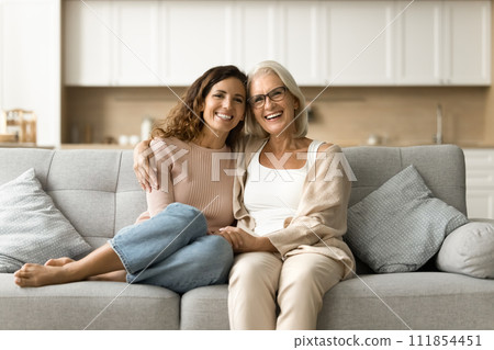 Cheerful senior mother and daughter woman sitting on home couch Cheerful senior mother and daughter woman sitting on home couch 111854451