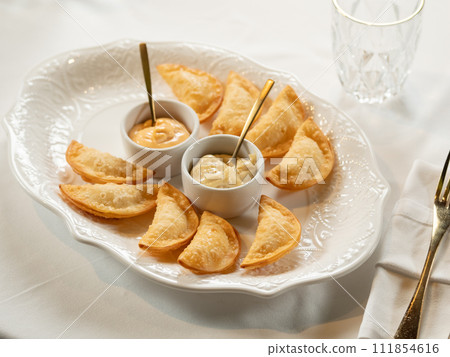 Hot Appetizers with Mini Chebureki and sauces Isolated on white table background. Restaurant Starter Menu with Crispy Burnt Turnovers, Pies or Samosa with Spicy Sause Close Up 111854616