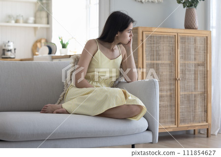 Sad pensive woman sits on sofa thinking about relationships Sad pensive woman sits on sofa thinking about relationships 111854627