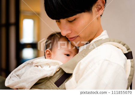 一位父親用嬰兒背帶抱著一個昏昏欲睡的嬰兒 111855070