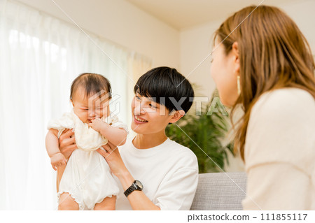 A family of three, a Japanese male father in his 30s holding a crying 0-year-old baby and a mother watching over him. A family of three, a Japanese male father in his 30s holding a crying 0-year-old baby and a mother watching over him. 111855117