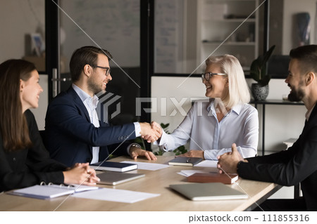 Positive senior business leader woman giving handshake to effective employee Positive senior business leader woman giving handshake to effective employee 111855316