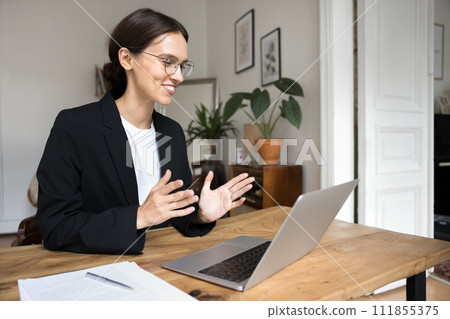 Positive young business professional woman speaking at laptop Positive young business professional woman speaking at laptop 111855375