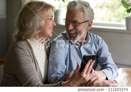 Joyful older spouses embrace relax with cell discuss funny video 111855574