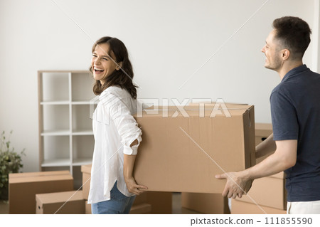 Joyful young married couple carrying large moving box 111855590