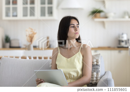 Pensive attractive young woman sitting on couch with digital tablet 111855601