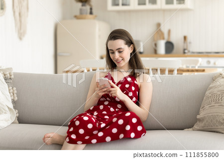 Pretty girl using smartphone seated on sofa in cozy apartment Pretty girl using smartphone seated on sofa in cozy apartment 111855800