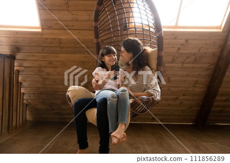 Latina mother relax on swing use smartphone with preteen daughter 111856289