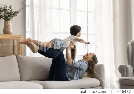 Loving mother lying on couch play with little adorable daughter 111856477