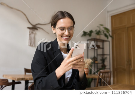Cheerful young businesswoman enjoying online communication on smartphone Cheerful young businesswoman enjoying online communication on smartphone 111856764