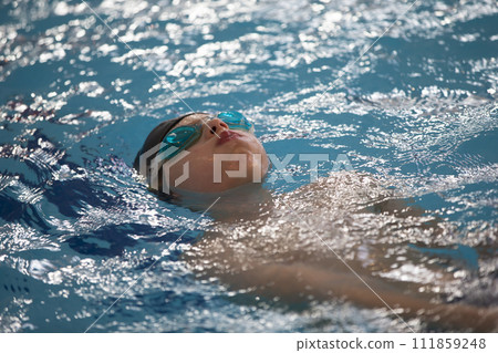 Boy in a swimming cap and swimming goggles in the pool. The child is engaged in the swimming section. Boy in a swimming cap and swimming goggles in the pool. The child is engaged in the swimming section. 111859248