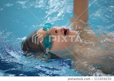 Boy in a swimming cap and swimming goggles in the pool. The child is engaged in the swimming section. 111859250