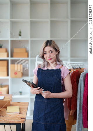 Portrait Of Asian Female Owner Of Fashion Store Checking Stock In Clothing Store With using notebook successful happy smile at small business, sme or ecommerce concepts. 111859275