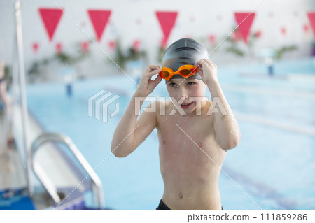 Boy in a swimming cap and swimming goggles in the pool. The child is engaged in the swimming section. Boy in a swimming cap and swimming goggles in the pool. The child is engaged in the swimming section. 111859286