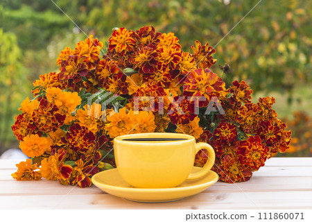 Summer leisure activities concept; yellow cup of coffee and bunch of orange marigold flowers on a wooden table in green garden 111860071