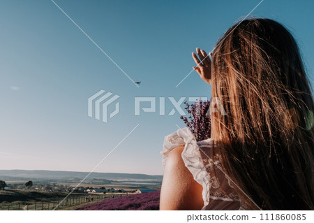 Woman lavender field. Happy carefree woman in a white dress walking in a lavender field and smelling a lavender bouquet on sunset. Ideal for warm and inspirational concepts in wanderlust and travel. Woman lavender field. Happy carefree woman in a white dress walking in a lavender field and smelling a lavender bouquet on sunset. Ideal for warm and inspirational concepts in wanderlust and travel. 111860085