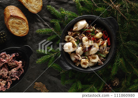 Fried  squid  with chilli pepper, garlic and butter served in iron cast pan on black textured background decorated with forest details. Christmas food decoration concept 111860980