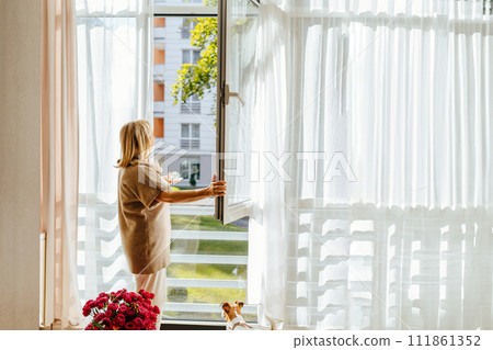 Woman having cup of coffee open the window, breathing fresh air, enjoy sunny day, looking outside. Woman having cup of coffee open the window, breathing fresh air, enjoy sunny day, looking outside. 111861352