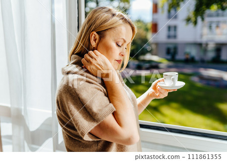 Relax, coffee and happy 55s blond woman at home thinking about peaceful memories and enjoying her free time feeling content and relax. Mature lady at peace with positive mindset in home. Relax, coffee and happy 55s blond woman at home thinking about peaceful memories and enjoying her free time feeling content and relax. Mature lady at peace with positive mindset in home. 111861355