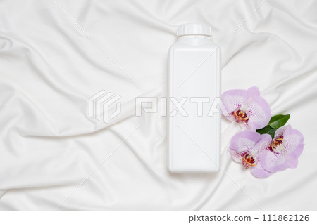 Liquid laundry detergent or fabric softener on bedding, orchid flowers, top view 111862126