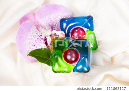Laundry capsules among orchid flowers on satin fabric. 111862127