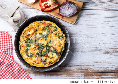Italian Frittata made with spinach, tomatoes, onion and peppers on white wooden table Italian Frittata made with spinach, tomatoes, onion and peppers on white wooden table 111862158