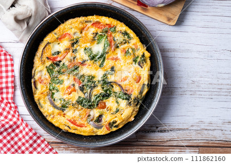 Italian Frittata made with spinach, tomatoes, onion and peppers on white wooden table 111862160
