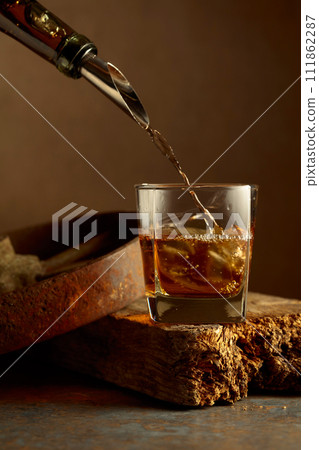 Whiskey is poured from a bottle into a frozen glass with natural ice. Whiskey is poured from a bottle into a frozen glass with natural ice. 111862287