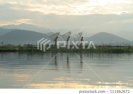 Burmese fisherman casting or throwing a net for catching freshwater fish in Unle lake, natural river in Asia in Myanmar. People lifestyle. 111862672