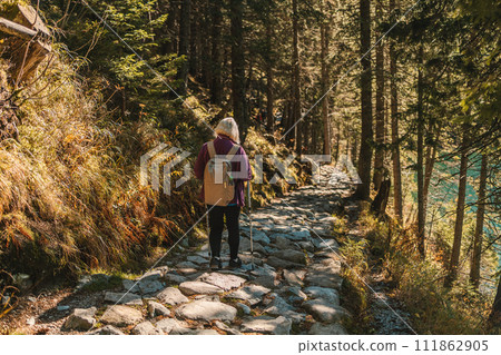 Mature caucasian blonde woman on vacation, having a hike in autumn mountains with backpack and hiking poles, enjoying adventure. Mature caucasian blonde woman on vacation, having a hike in autumn mountains with backpack and hiking poles, enjoying adventure. 111862905