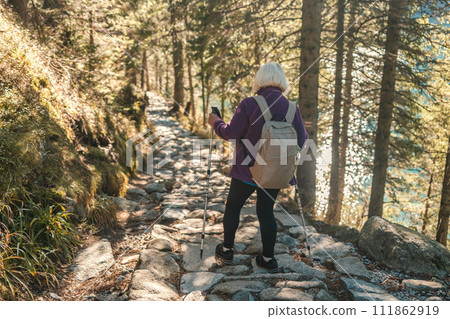 Mature caucasian blonde woman on vacation, having a hike in autumn mountains with backpack and hiking poles, enjoying adventure. 111862919