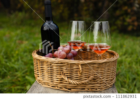 Close up of basket grape fruits, glass of red wine on green grass in garden. Summer weekend outdoor.  111862931
