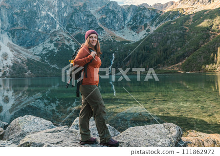 Shot of woman traveler relaxing alone travel in adventure vacation with backpack enjoying standing on the top of the mountain near Famous mountains lake Morskie oko or sea eye lake In High Tatras Shot of woman traveler relaxing alone travel in adventure vacation with backpack enjoying standing on the top of the mountain near Famous mountains lake Morskie oko or sea eye lake In High Tatras 111862972