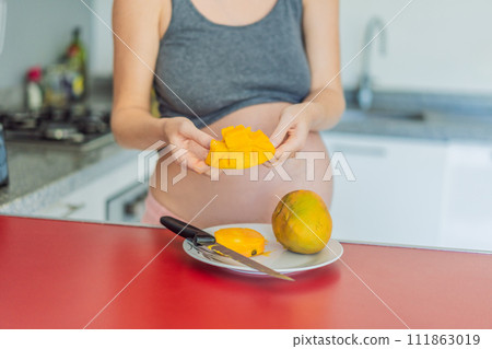 A skillful pregnant woman delicately cuts into a ripe mango, savoring a moment of culinary joy and nourishing her pregnancy with a fresh and flavorful treat 111863019